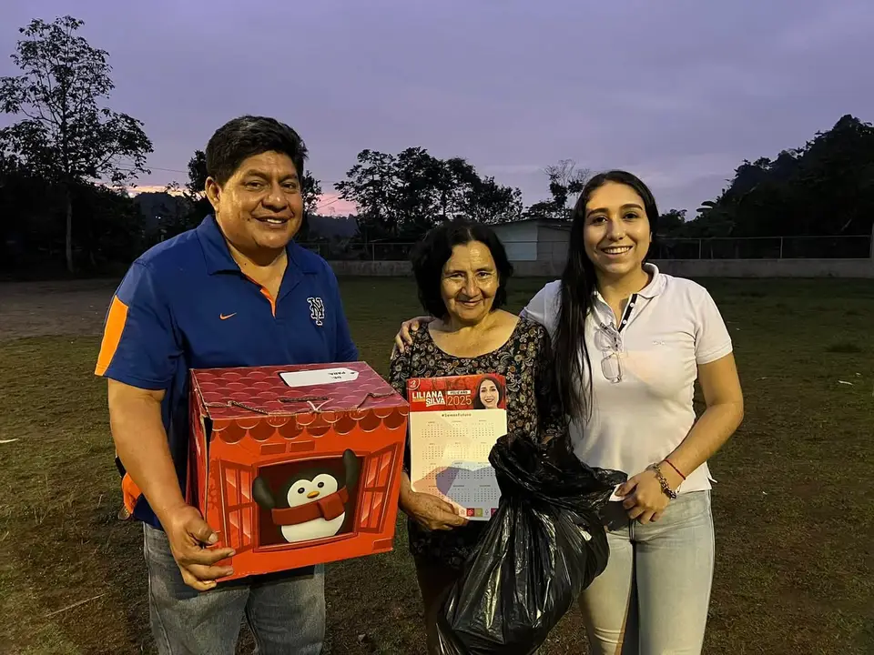 La autora posa junto a dos personas adultas; sostienen un calendario de 2025 y se observan una caja y una bolsa.