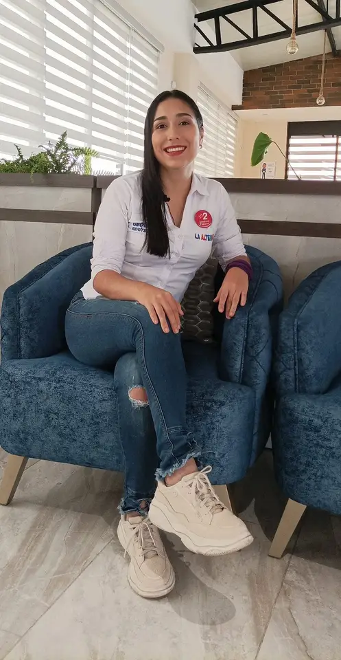 Liliana sentada en un sillón dentro de un espacio interior.