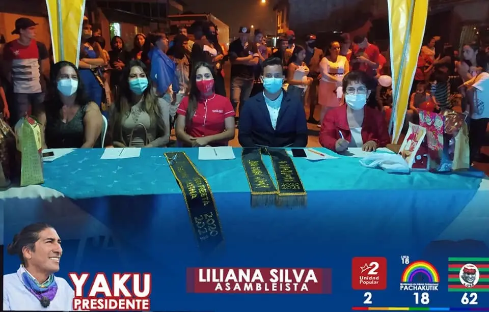 Personas sentadas detrás de una mesa decorada durante un evento nocturno con luces azules y globos rojos.