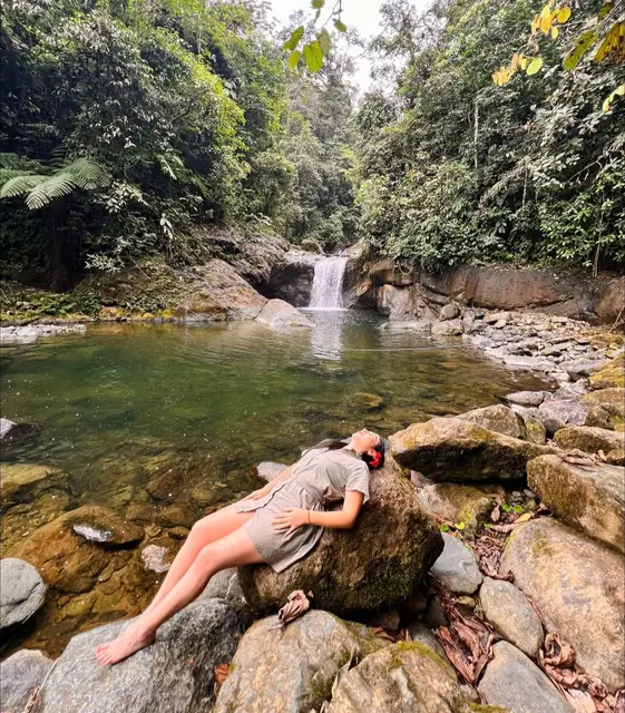 Cascada y poza de agua en un bosque tropical de El Esfuerzo; Liliana aparece recostada sobre una roca.
