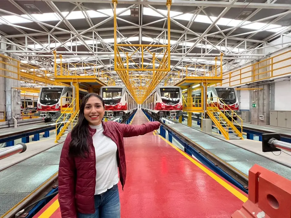 Liliana posa delante de varios trenes dentro de una instalación ferroviaria.