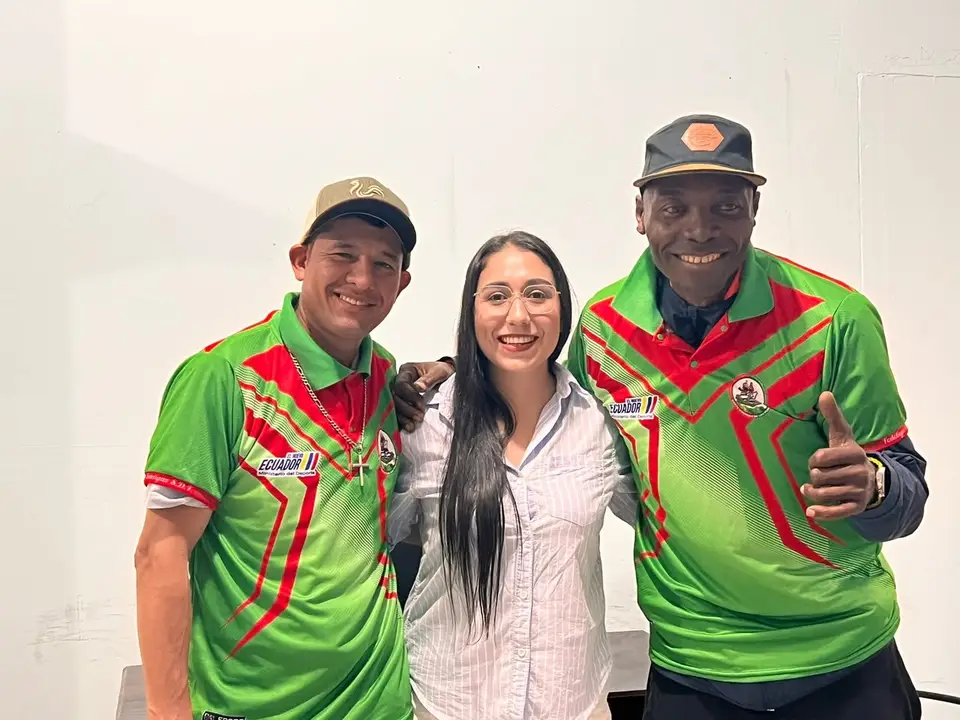 Dos deportistas uniformados posan junto a una mujer frente a un panel del Ministerio del Deporte.