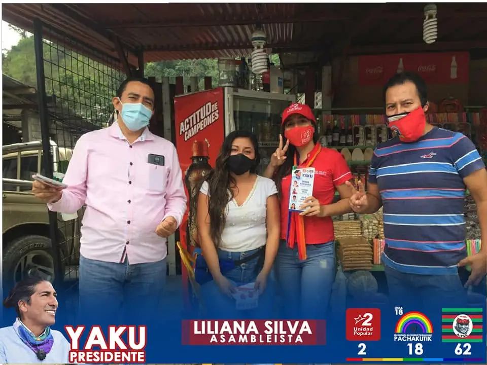 Cuatro personas posan frente a un local; una sostiene un folleto y otra hace una señal de paz.