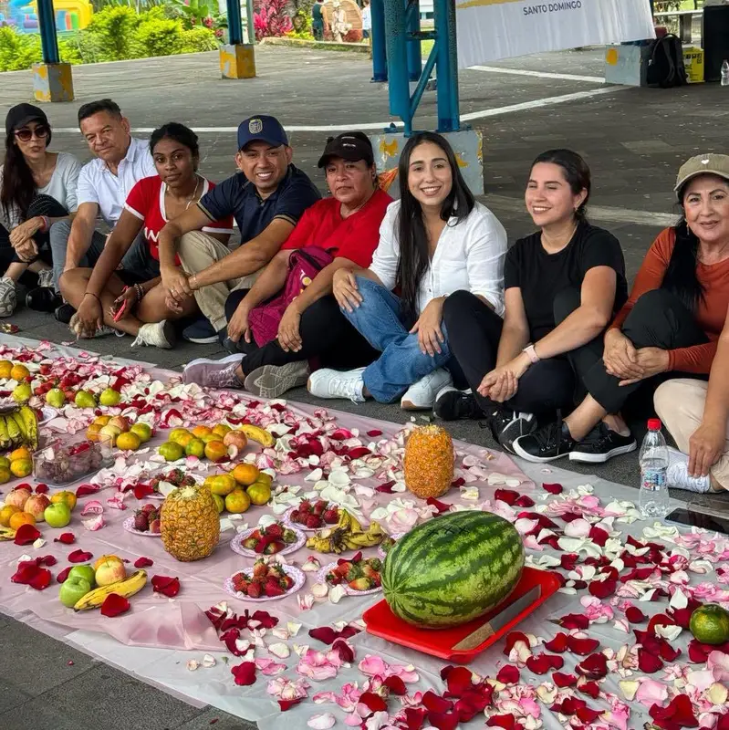 Personas sentadas junto a una mesa comunitaria cubierta de frutas, flores y pétalos.