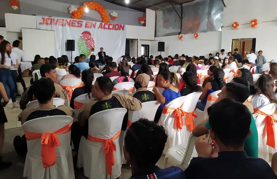 Reunión de jóvenes en un salón decorado con globos naranjas y el letrero «Jóvenes en Acción».
