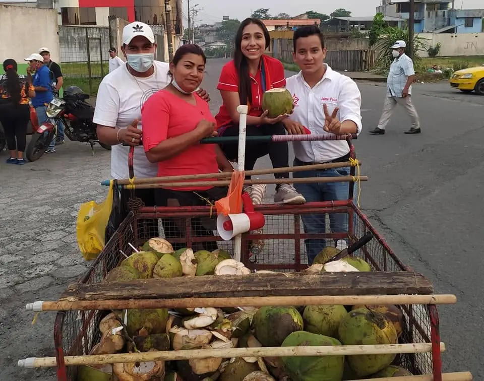 Cuatro personas posan junto a un carrito cargado de cocos en una calle.
