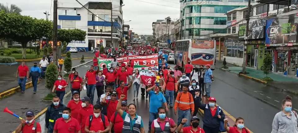 Marcha numerosa con pancartas recorre una avenida urbana; se observan autobuses.