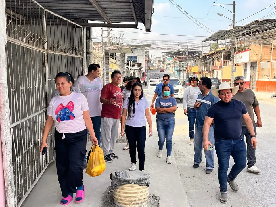 Grupo de personas camina por una acera junto a una calle con vehículos y cableado.