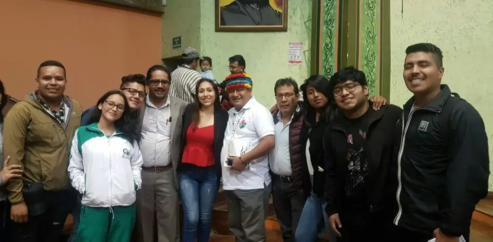 Grupo de personas posa en un salón; una de ellas lleva un sombrero multicolor.