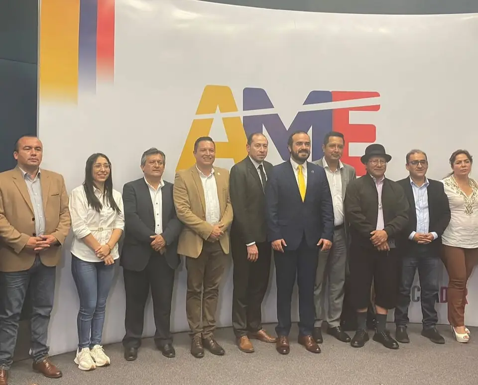 La autora posa con integrantes de la AME en un salón frente a un panel con las siglas AME.