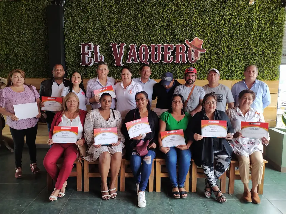 Grupo de personas posa en un local; varias sostienen certificados de reconocimiento.
