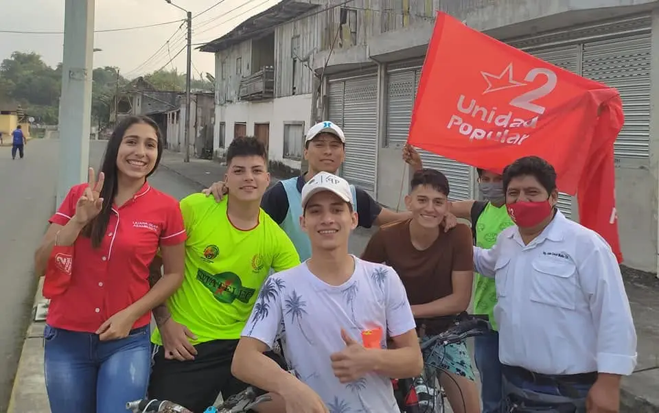 Grupo de personas posa en una calle junto a una bandera roja.