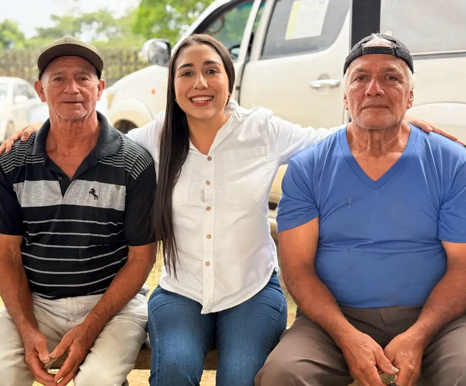 La autora posa con dos hombres adultos junto a un vehículo.